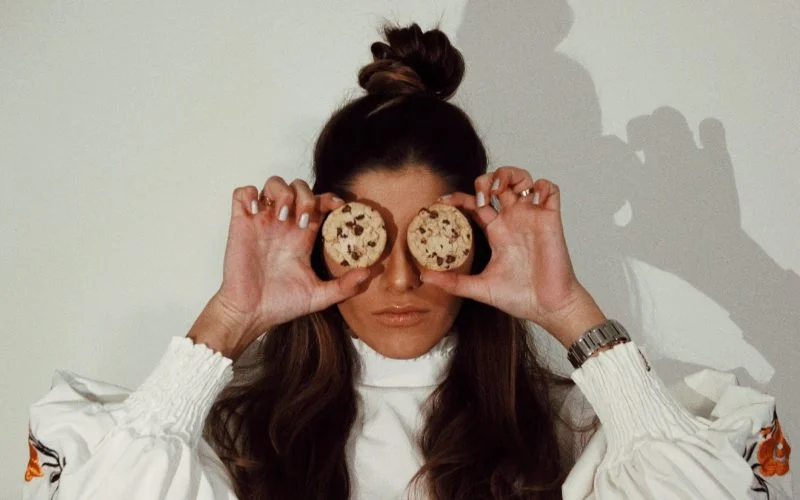 woman covering eyes with two chocolate chip cookies